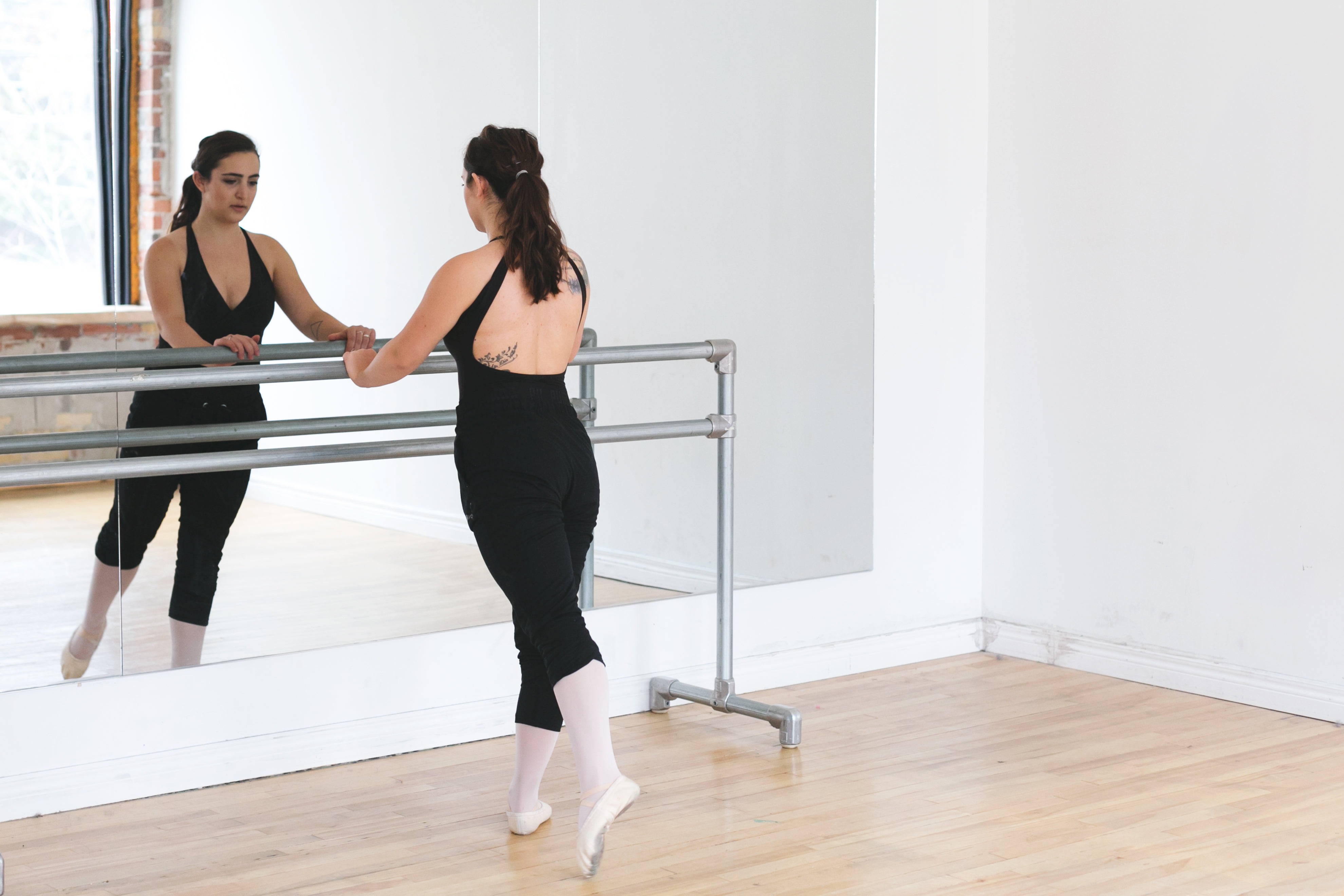 A ballet dancer practicing at the barre in front of a studio mirror